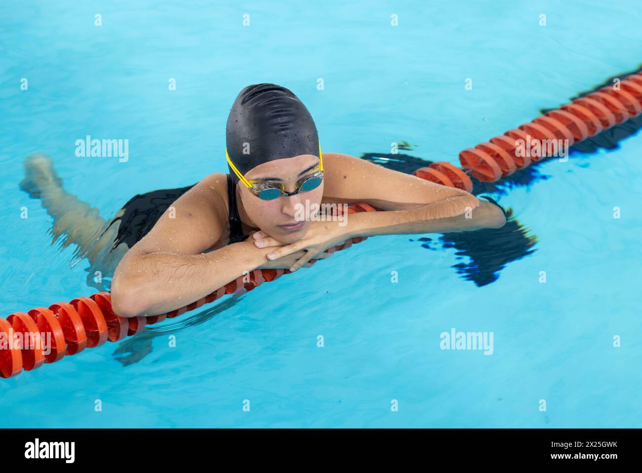 Biracial jeune femme nageuse s'entraînant à l'intérieur dans la piscine, portant un chapeau noir et des lunettes Banque D'Images