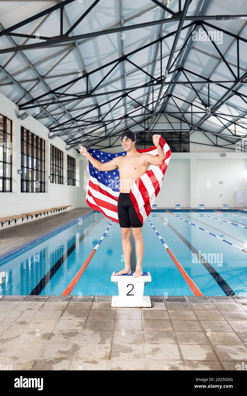 Jeune nageur caucasien tenant le drapeau américain se tient près de la piscine à l'intérieur Banque D'Images