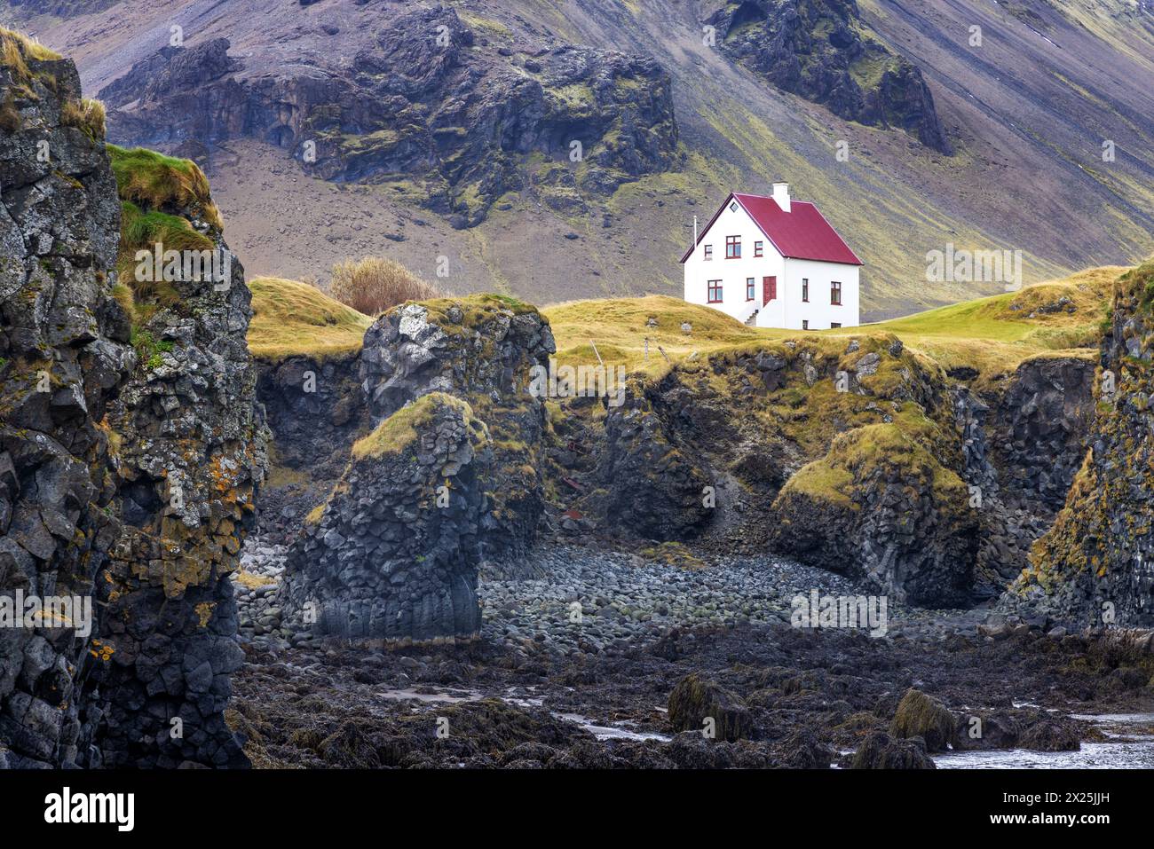 Arnarstapi, Islande. Une vue sur la côte escarpée avec une maison solitaire. Couleurs d'automne avec des montagnes en arrière-plan. Péninsule de Snaefellsnes. Banque D'Images