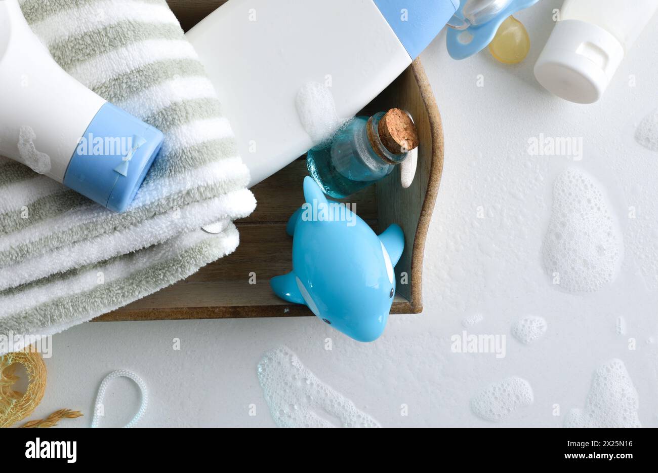 Soins de bébé pour le bain avec des détails d'accessoires et de produits sur la table blanche avec de l'eau et de la mousse. Vue de dessus. Banque D'Images