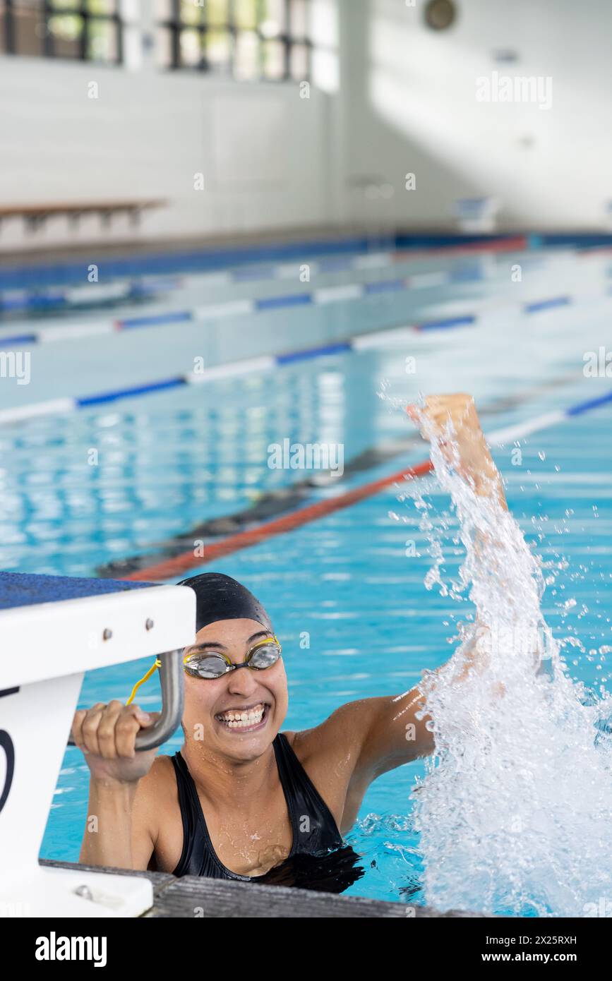 Biracial jeune femme nageuse portant des lunettes célébrant à l'intérieur dans la piscine, espace de copie Banque D'Images