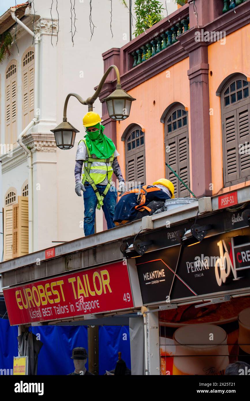 Deux hommes peignent le toit métallique d'un auvent un dimanche à Campbell Lane Singapour (Little India) avec une chaleur de 35 degrés et 97% d'humidité. Banque D'Images