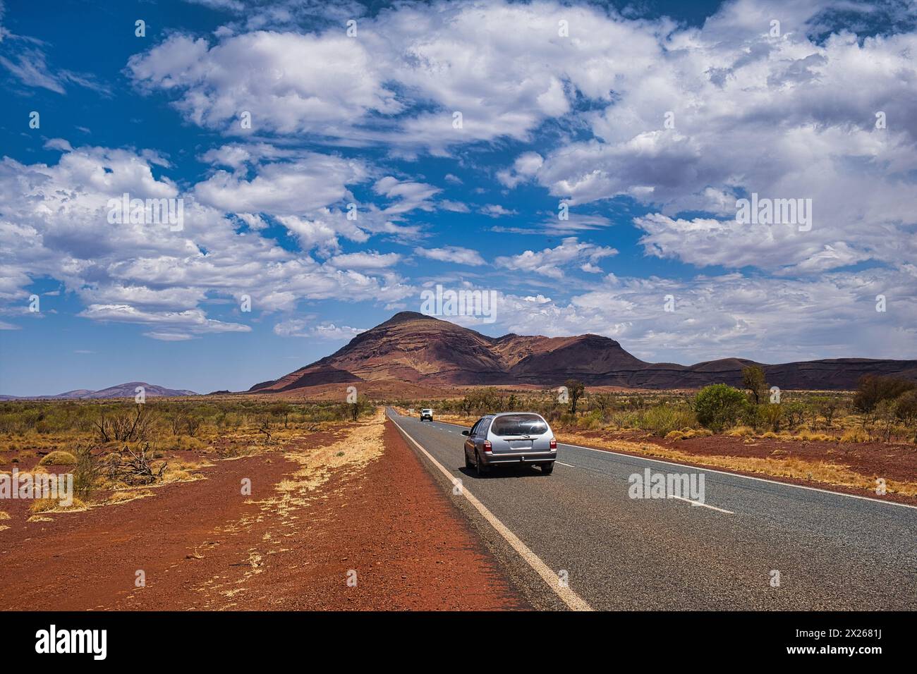 Autoroute avec deux voitures dans l'arrière-pays reculé du parc national de Karijini. Vue sur le mont Bruce, la deuxième plus haute montagne d'Australie occidentale. Banque D'Images