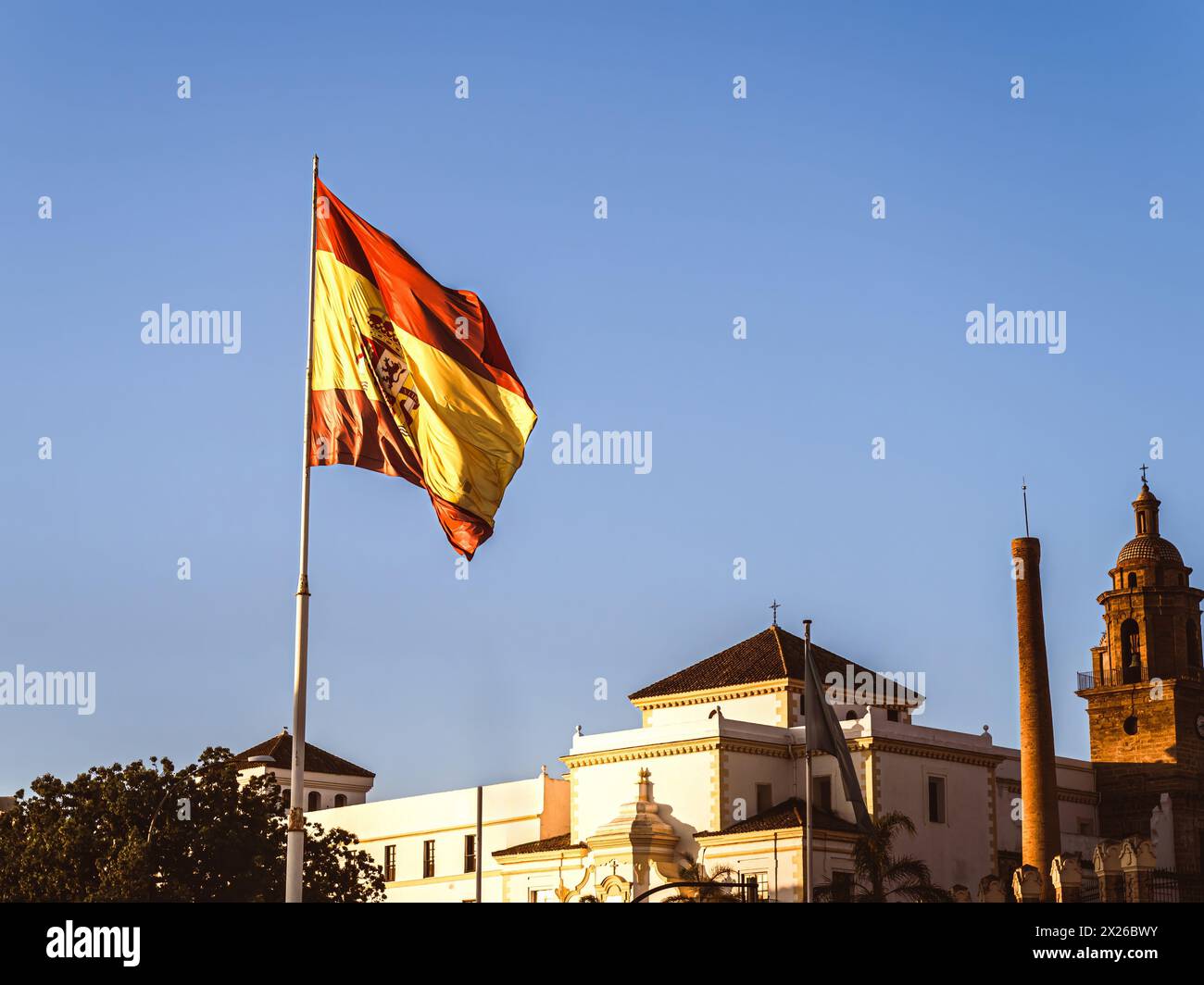 Un drapeau espagnol qui survole la ville de Cadix pendant l'heure d'or du matin, en été Banque D'Images