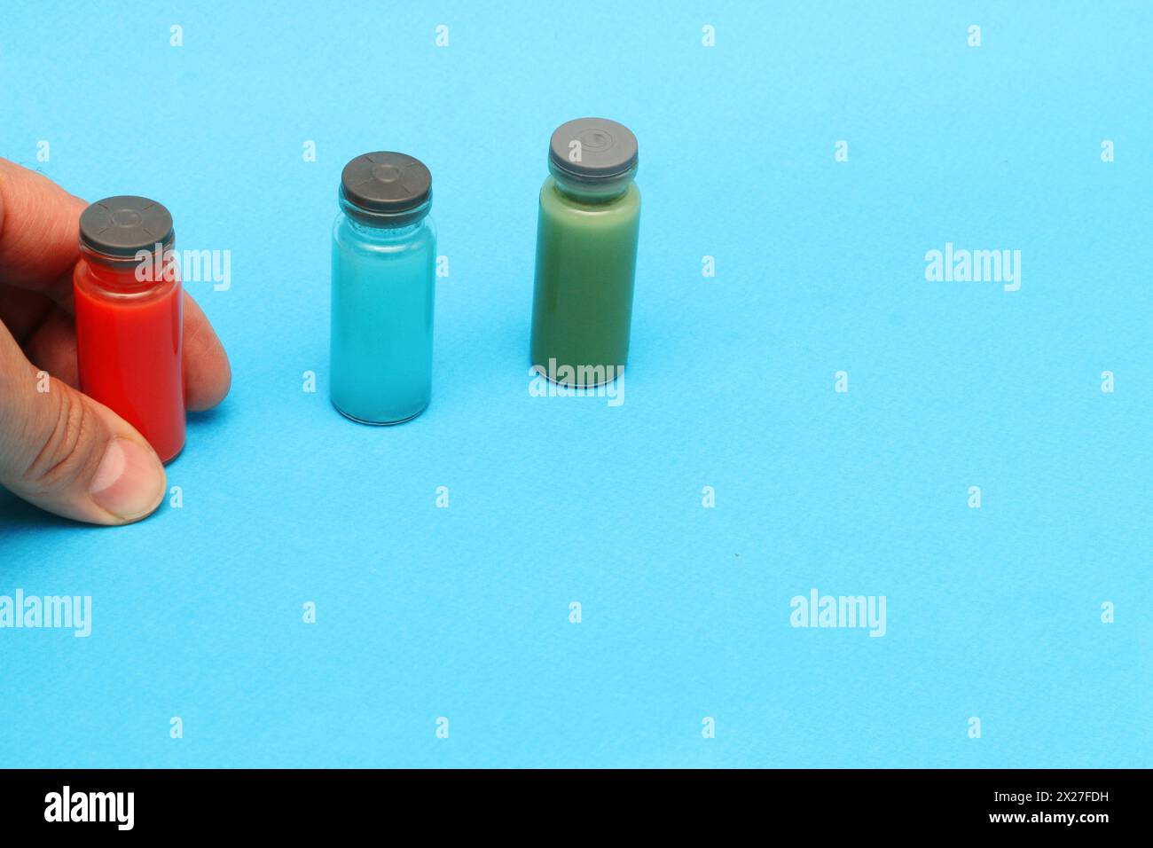 La main d'un homme tient une bouteille avec un test sanguin, des bouteilles bleues et vertes avec des réactifs chimiques sur un fond bleu..... Banque D'Images