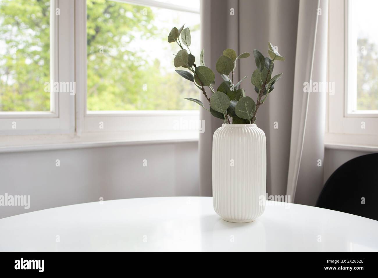 Fond de vase blanc avec eucalyptus artificiel sur table blanche et fenêtre à l'arrière Banque D'Images