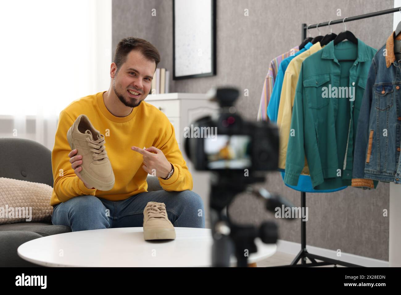 Blogueur de mode souriant montrant des chaussures tout en enregistrant une vidéo à la maison Banque D'Images