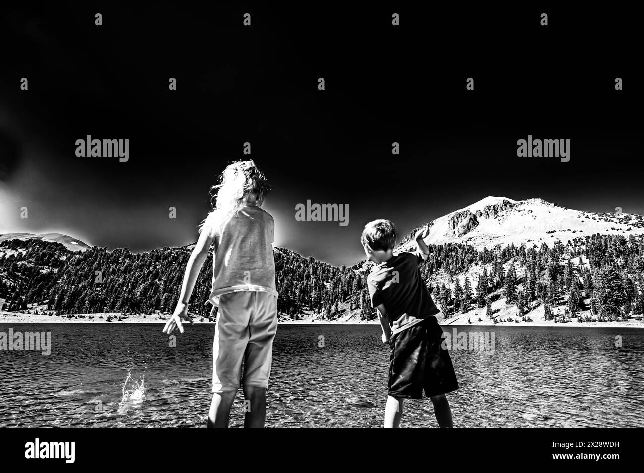 Enfants jetant des rochers du bord de l'eau du lac Helen dans le parc national volcanique de Lassen, Californie. Banque D'Images