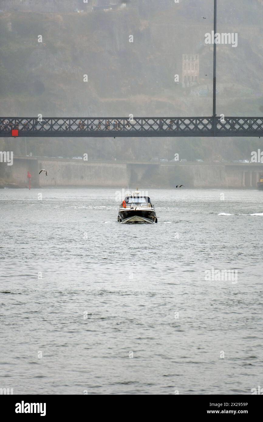 Bateau naviguant sous la plate-forme inférieure du pont en acier Don Luis, avec des gens marchant avec des parapluies en raison de la pluie légère et du brouillard qui l'entoure Banque D'Images