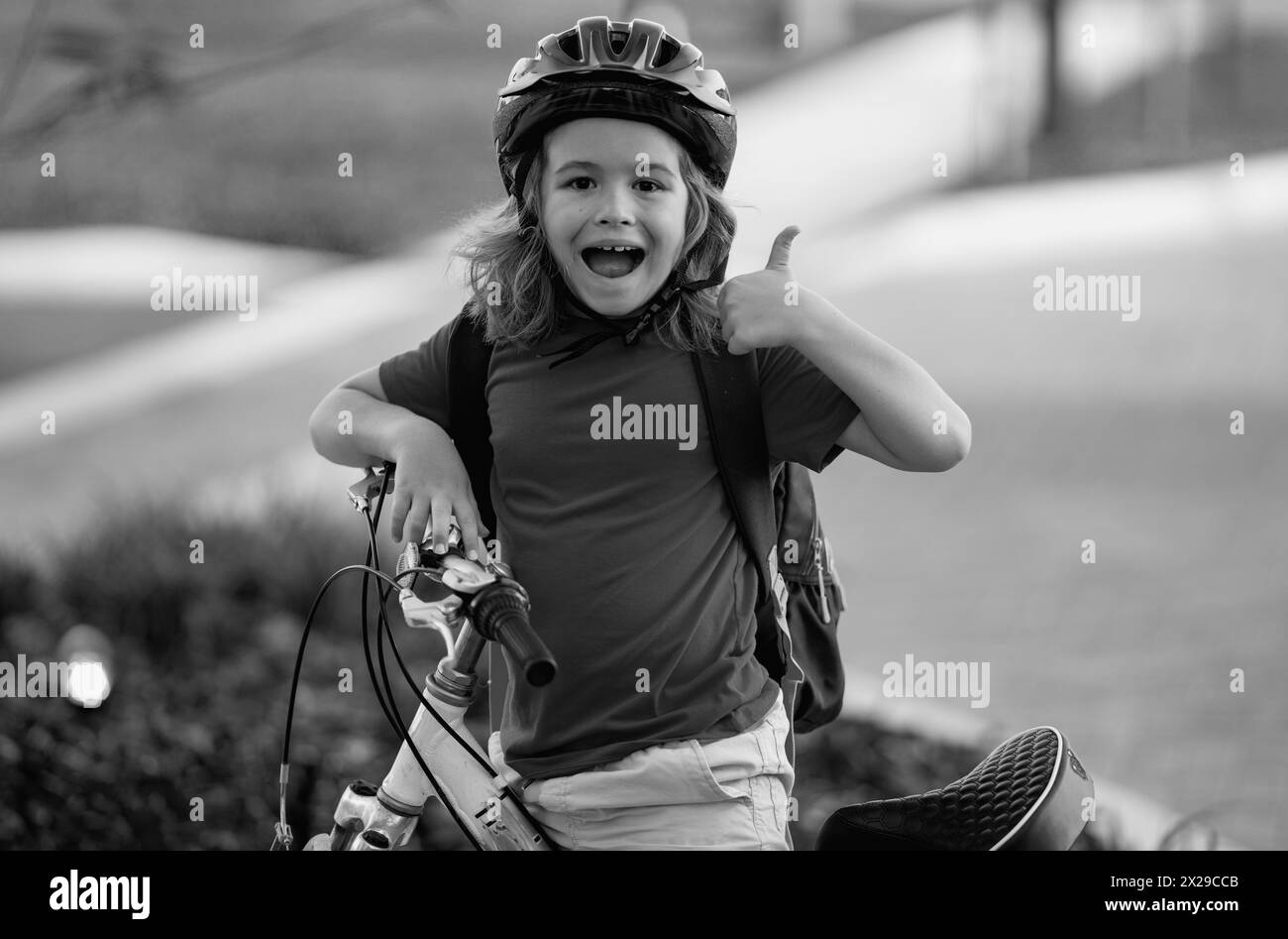 Enfant à vélo. Petit garçon dans un casque à vélo le long d'une piste cyclable. Joyeux petit garçon à vélo dans le parc d'été. Enfant en protection Banque D'Images