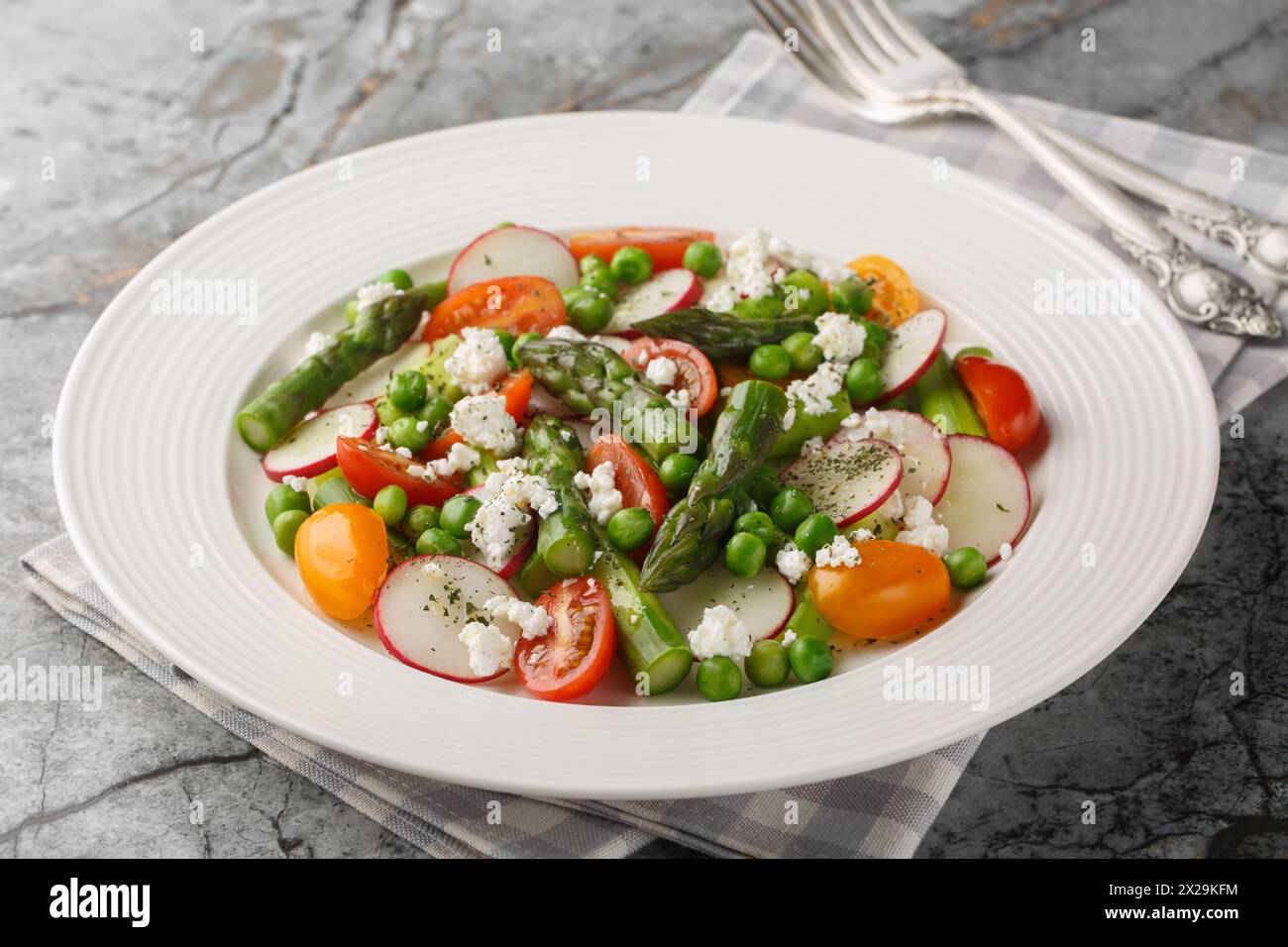 Salade d'asperges, radis, tomates cerises, pois verts et fromage de chèvre habillé de vinaigrette gros plan dans une assiette sur la table. Horizontal Banque D'Images
