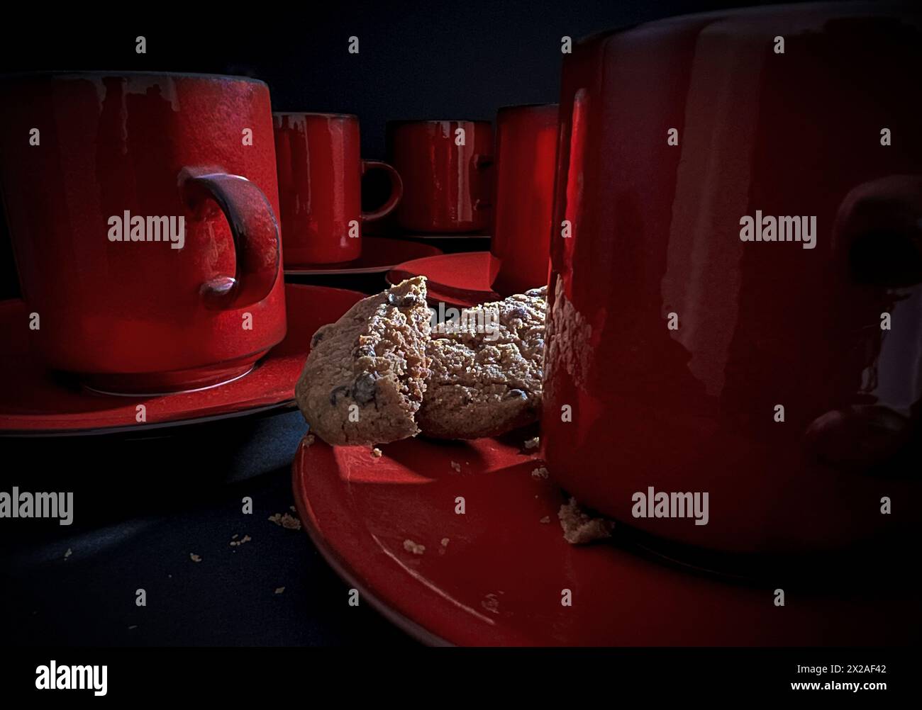 Tasses à café rouges avec biscuit cassé sur soucoupe avec fond sombre Banque D'Images Tasses à café rouges avec biscuit cassé sur soucoupe avec fond sombre Banque D'Images