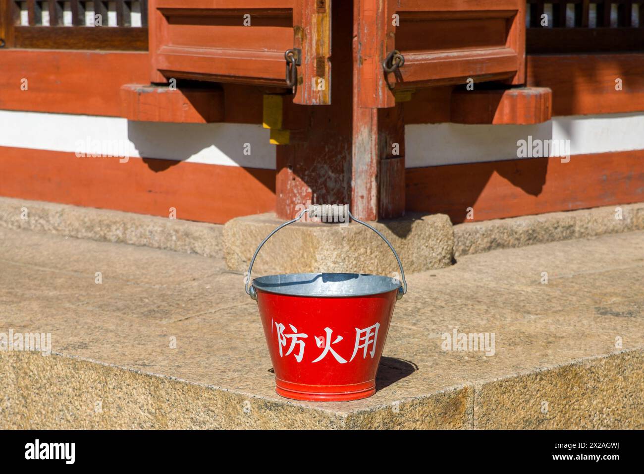 un seau rouge avec l'inscription japonaise 'pour la protection contre l'incendie' devant un vieux bâtiment en bois Banque D'Images
