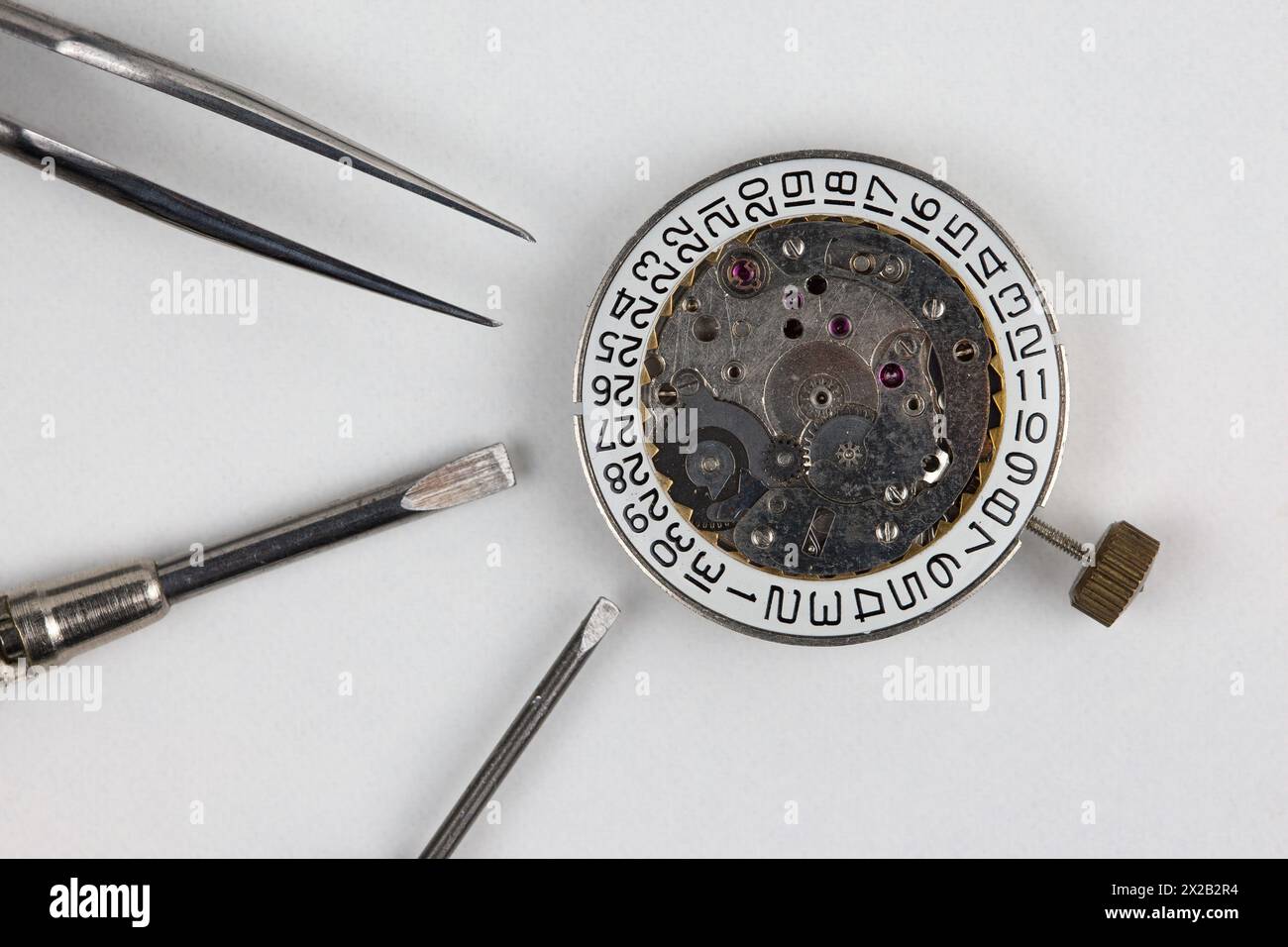 Une horloge, deux tournevis et une paire de pinces reposent sur l'établi blanc - une scène débordant de précision et de mécanique fine. Banque D'Images