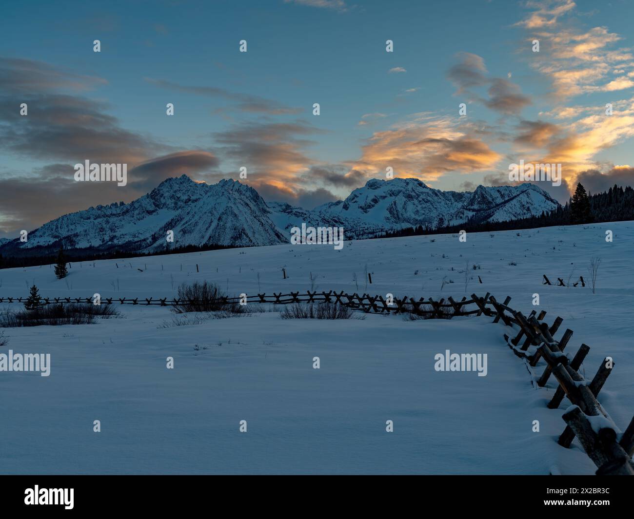La neige et la barrière de poteau mènent à un beau coucher de soleil sur la chaîne de montagnes Banque D'Images