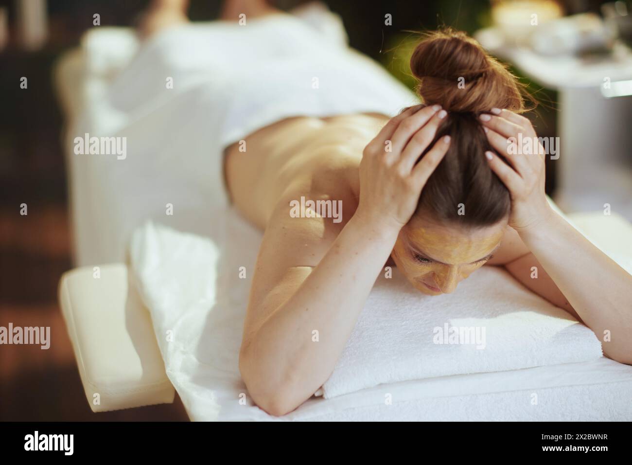 Temps de soins. femme d'âge moyen moderne stressée dans une armoire de massage avec masque cosmétique doré sur le visage posé sur la table de massage. Banque D'Images