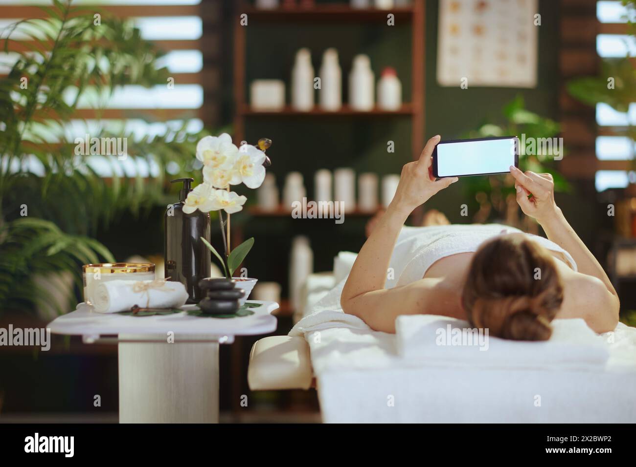 Temps de soins. femme moderne détendue dans l'armoire de massage avec téléphone portable à écran blanc posé sur la table de massage. Banque D'Images