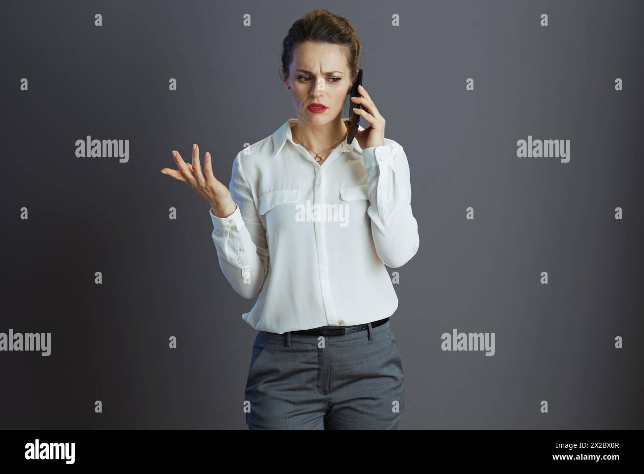 stressée travailleuse élégante de 40 ans en blouse blanche à l'aide d'un téléphone portable isolé sur gris. Banque D'Images