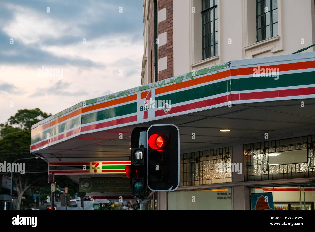Une scène urbaine se déroule à Adélaïde tandis que l'emblématique panneau Seven Eleven brille au milieu d'un feu rouge, projetant une ambiance tamisée Banque D'Images