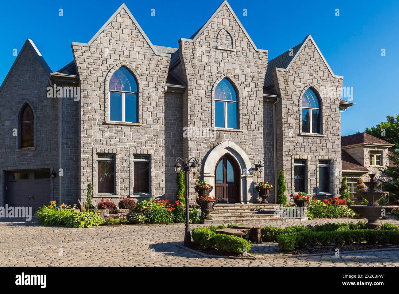 Façade de maison de style gothique en pierre taillée nuancée grise de deux étages avec cour avant paysagée en été. Banque D'Images