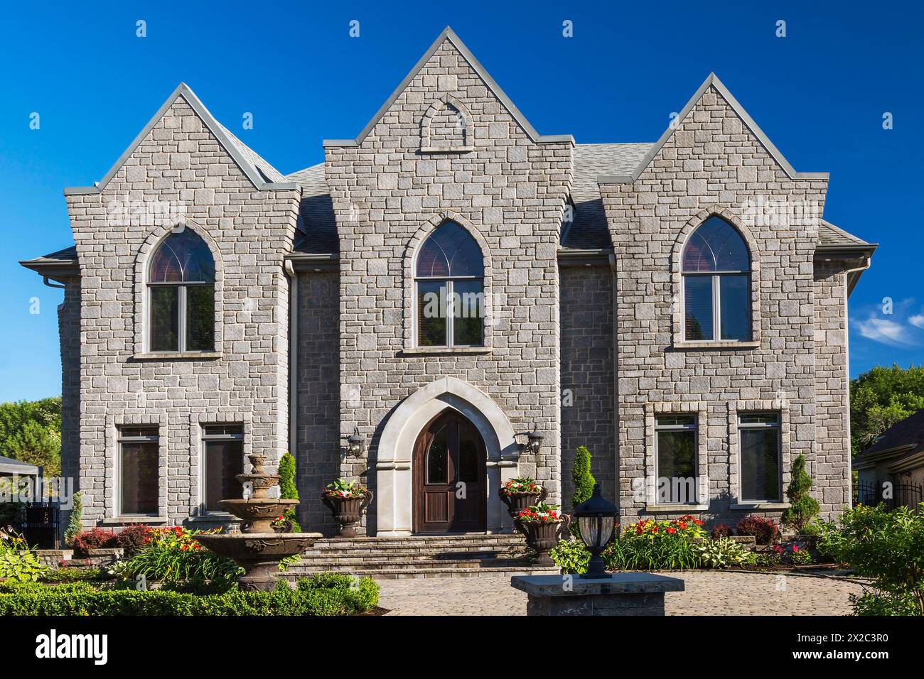 Façade de maison de style gothique en pierre taillée nuancée grise de deux étages avec cour avant paysagée en été. Banque D'Images