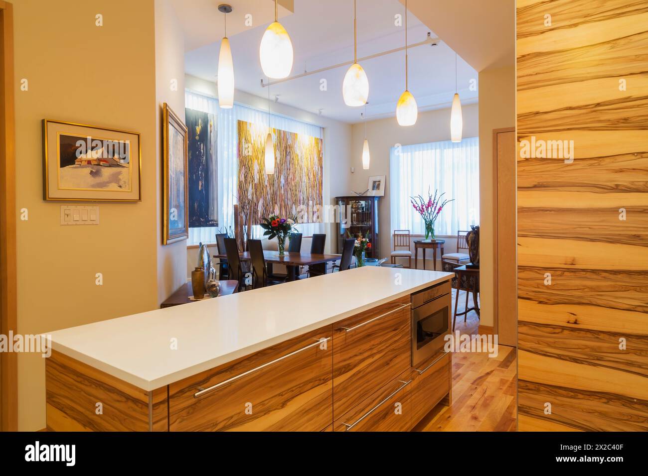 Îlot en bois de Gumwood avec comptoir en quartz blanc pur dans la cuisine avec érable, parquet en bois de cerisier plus table en bois de rose avec chaises à dossier haut en cuir noir. Banque D'Images