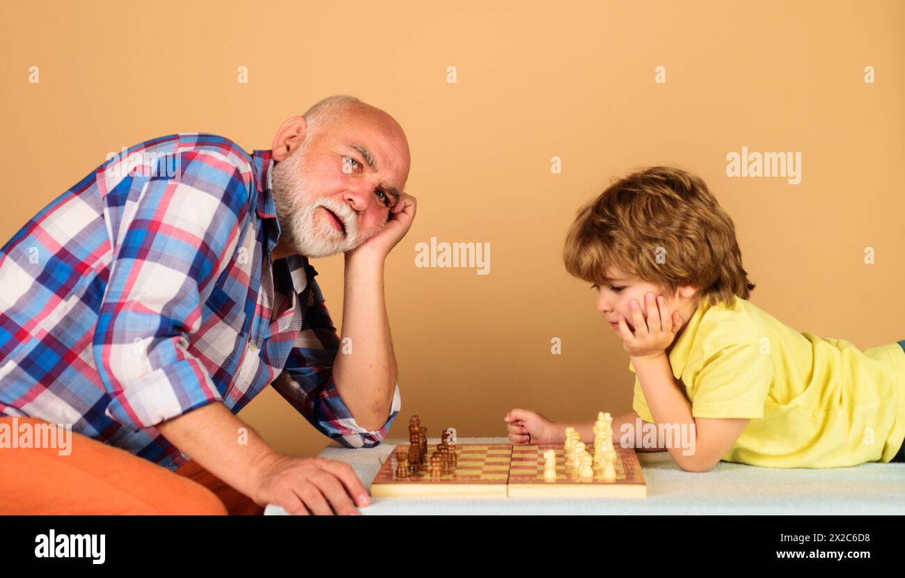 Garçon mignon avec grand-père jouant aux échecs ensemble à la maison. Enfants et jeux de logique de société. Grand-père et petit-fils jouent aux échecs. Passe-temps et loisirs Banque D'Images