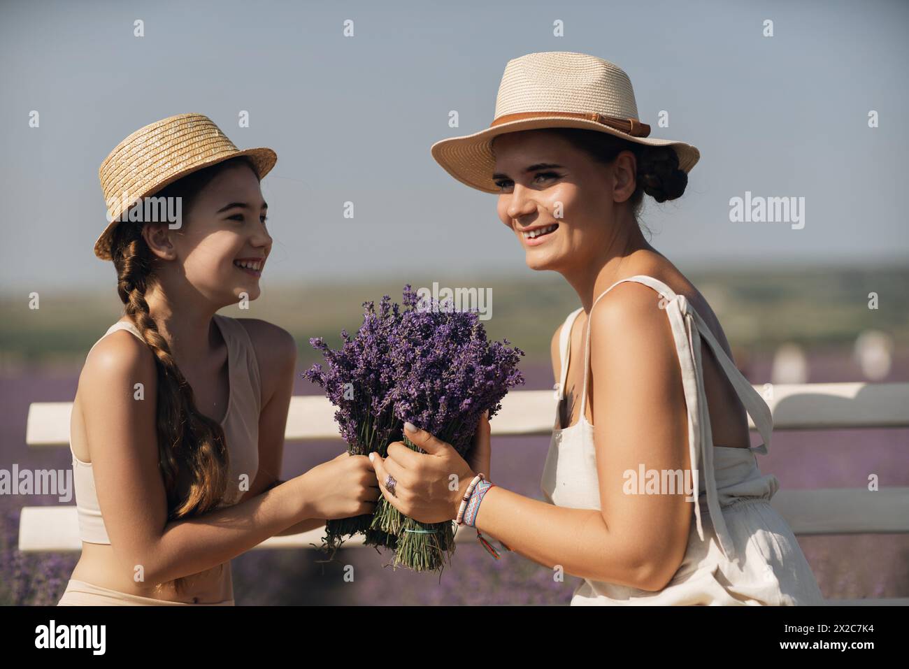 Une femme et un enfant sont assis sur un banc dans un champ de fleurs violettes lavande. La femme tient un bouquet de fleurs et l'enfant tient un Banque D'Images