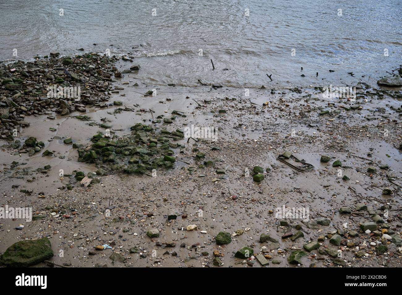 Regardant vers le bas les petites vagues se brisant sur les rochers et les pierres sur la rive de la rivière à marée basse Banque D'Images