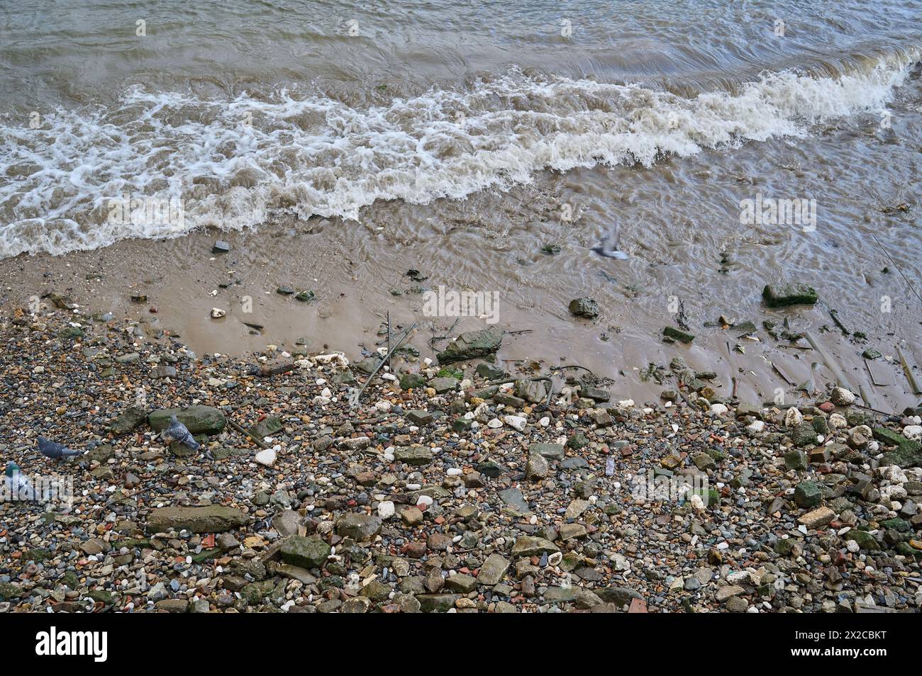 Regardant vers le bas les petites vagues se brisant sur les rochers et les pierres sur la rive de la rivière à marée basse Banque D'Images
