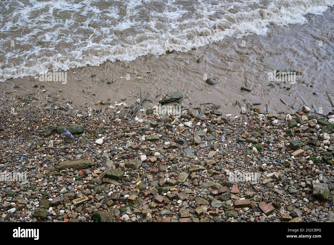 Regardant vers le bas les petites vagues se brisant sur les rochers et les pierres sur la rive de la rivière à marée basse Banque D'Images