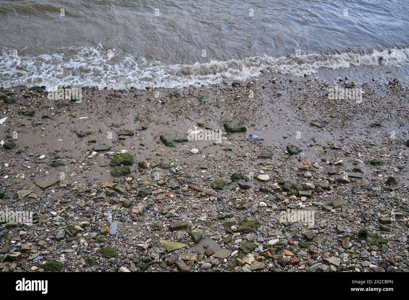 Regardant vers le bas les petites vagues se brisant sur les rochers et les pierres sur la rive de la rivière à marée basse Banque D'Images