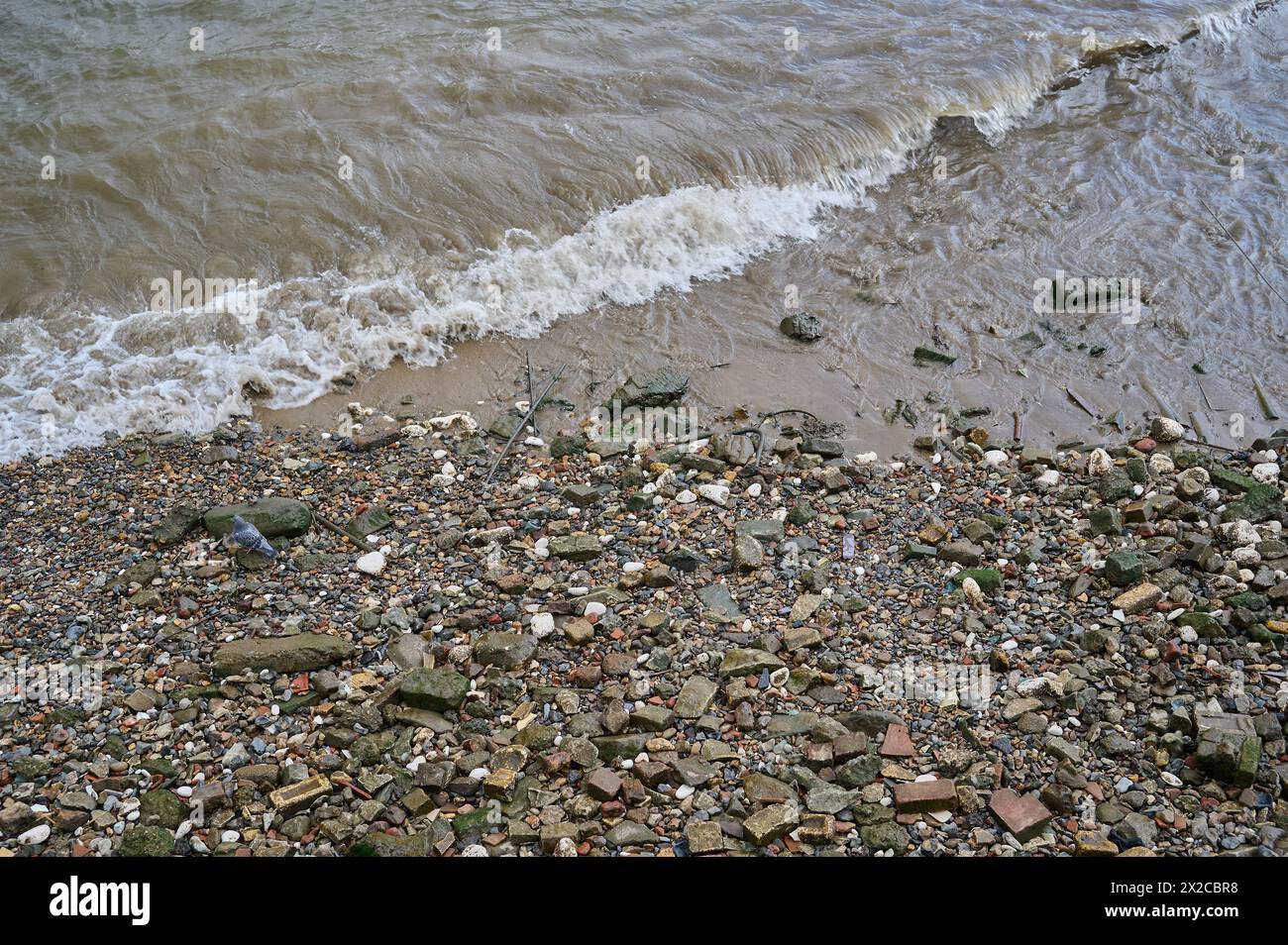 Regardant vers le bas les petites vagues se brisant sur les rochers et les pierres sur la rive de la rivière à marée basse Banque D'Images