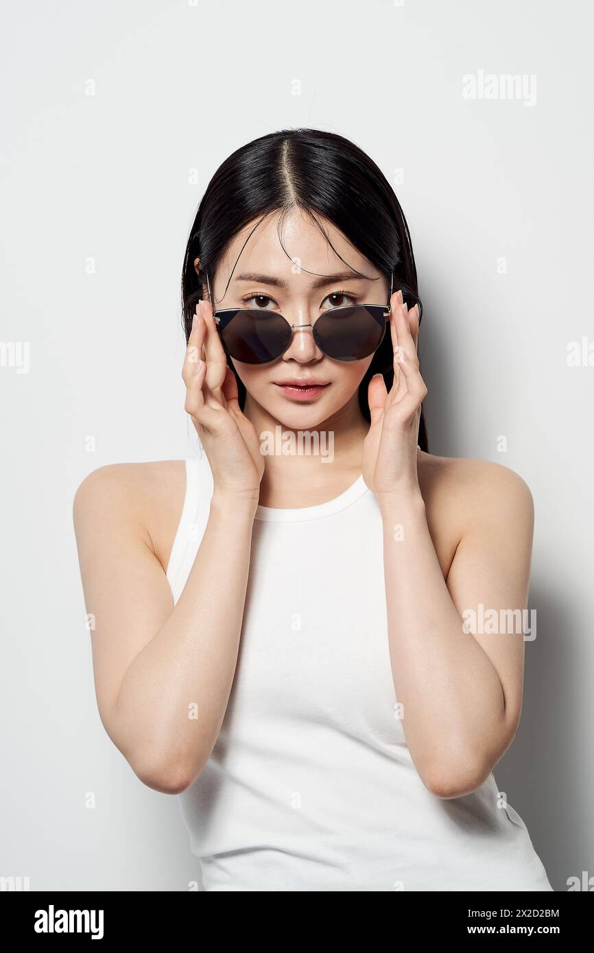 Femme asiatique regardant droit devant avec ses lunettes de soleil légèrement baissées avec les deux mains Banque D'Images