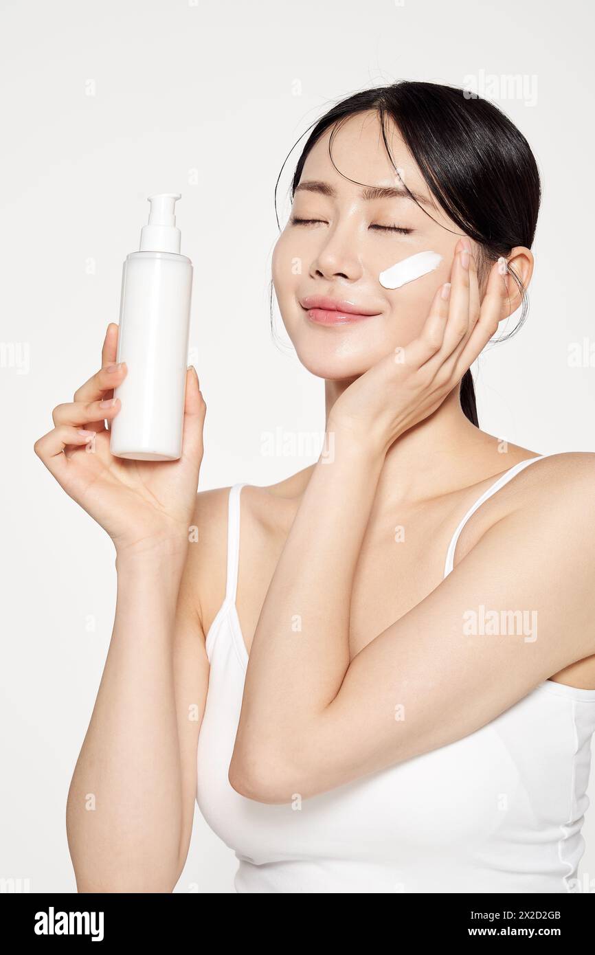 Femme asiatique pose pour appliquer des cosmétiques sur son visage Banque D'Images