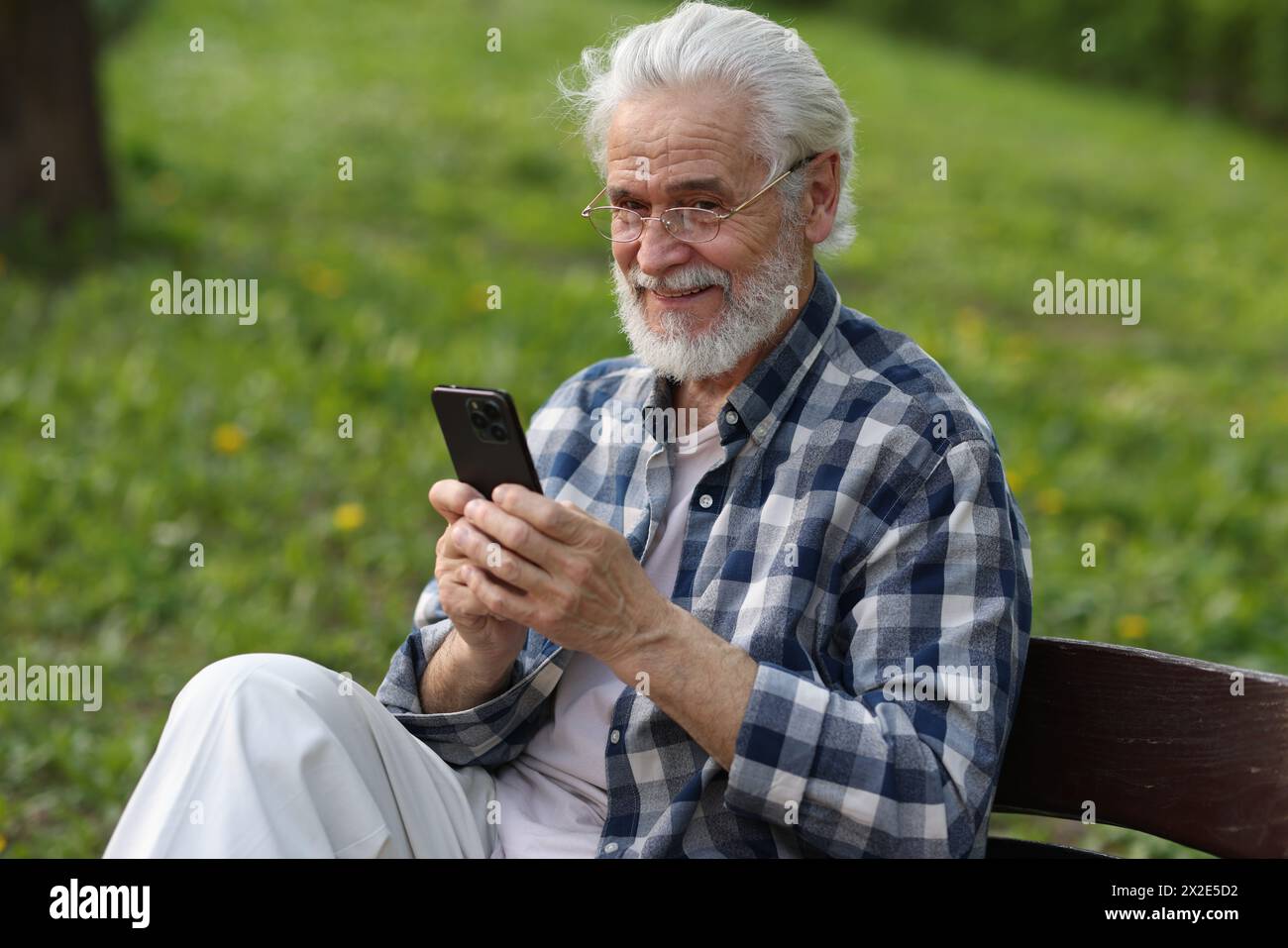 Portrait de grand-père heureux avec des lunettes à l'aide d'un smartphone sur le banc dans le parc Banque D'Images