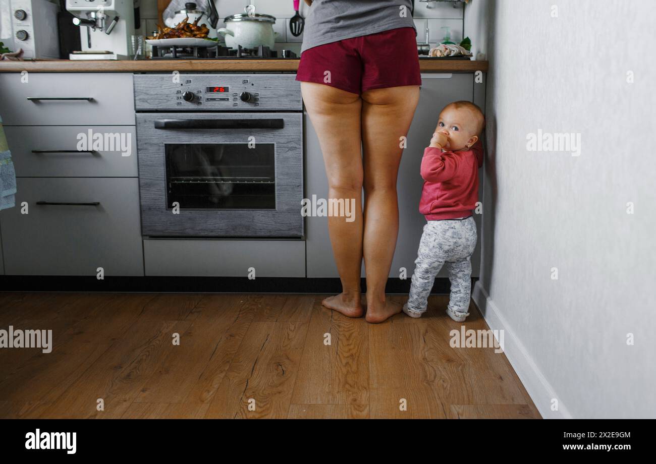 Un petit enfant se tient à côté de sa mère dans la cuisine. Banque D'Images