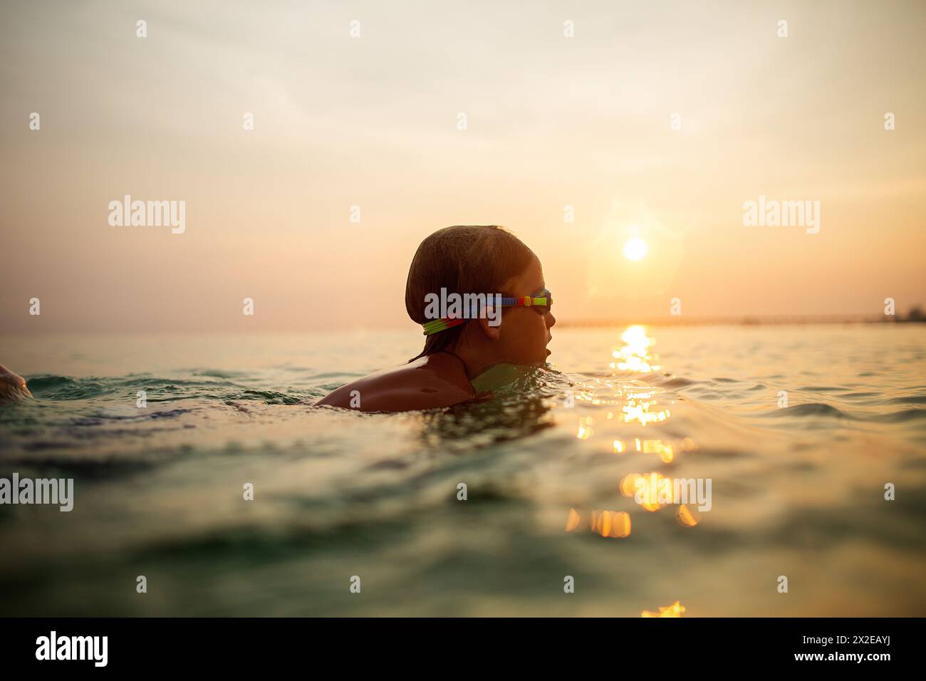 Enfant calme avec des lunettes nageant au coucher du soleil sur l'océan Banque D'Images