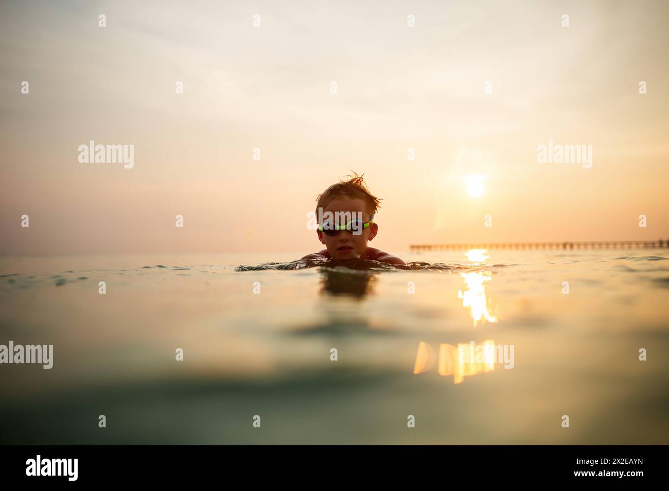Enfant dans des lunettes aime nager sereinement dans l'océan au coucher du soleil Banque D'Images