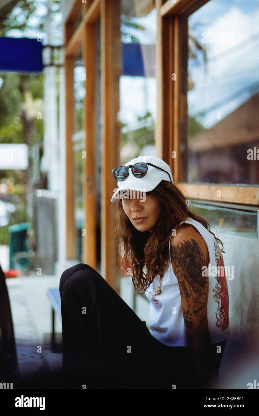 Jeune femme tatouée souriante assise sur un banc, photo de rue. Banque D'Images