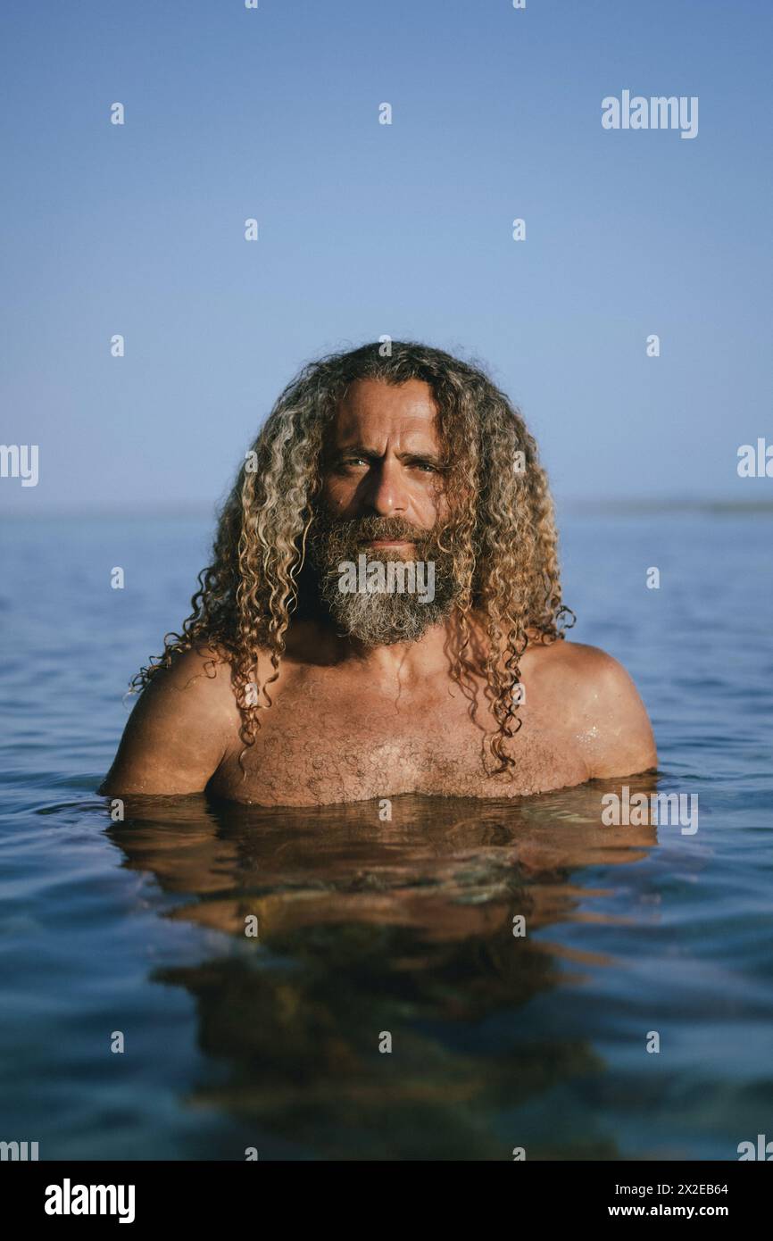 Un homme aux longs cheveux bouclés nage dans l'océan. Banque D'Images
