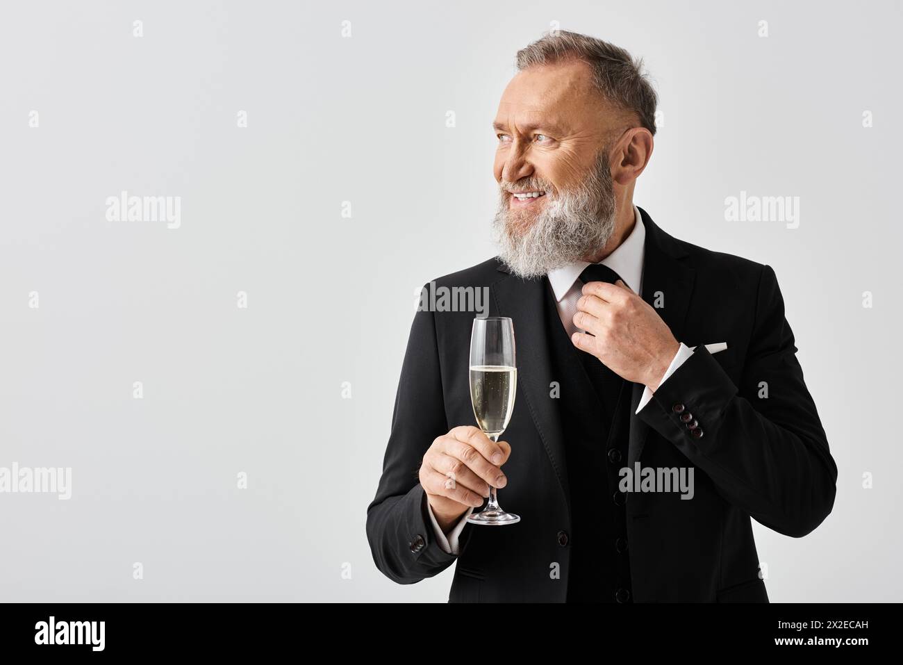 Un marié d'âge mûr dans un costume élégant tenant une coupe de champagne le jour de son mariage, exsudant sophistication et célébration. Banque D'Images