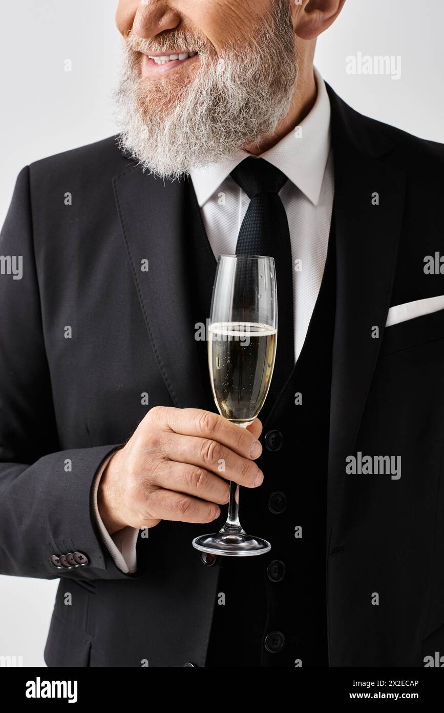 Marié d'âge mûr dans un costume élégant tenant gracieusement une coupe de champagne, exsudant sophistication et classe le jour de son mariage. Banque D'Images