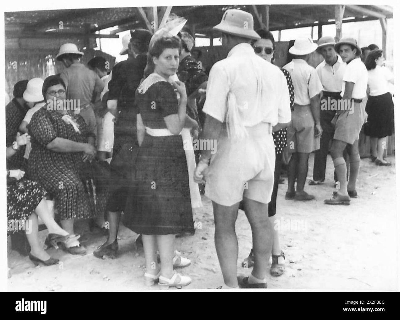 Dans un camp d'internés italiens, les internés et les visiteurs échangent leurs salutations pendant la journée de visite, reflétant une interaction sociale contrôlée sous la supervision de l'armée britannique. Banque D'Images