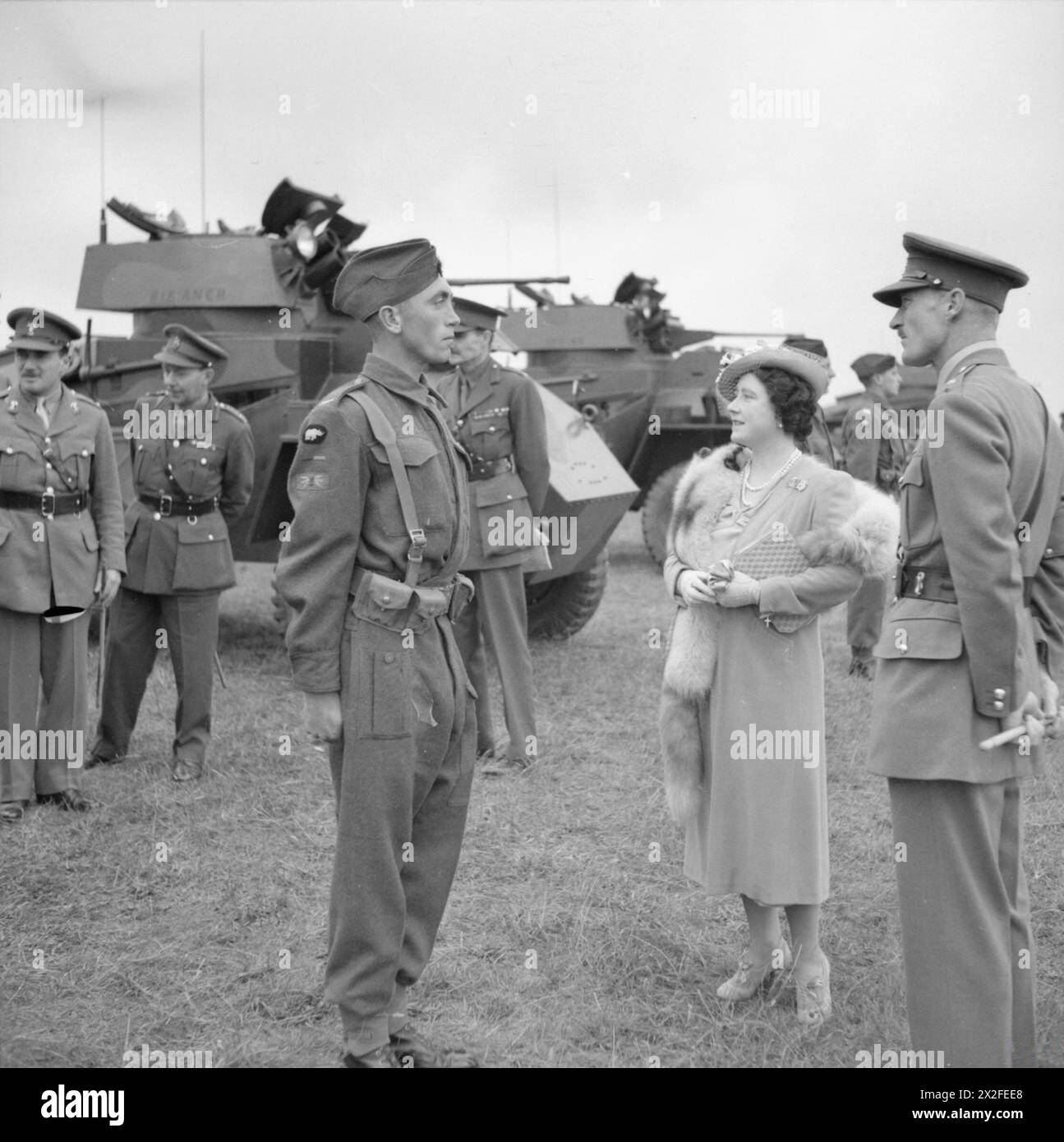La reine Elizabeth inspecte les équipages de véhicules blindés de la 12e Royal Lancers, 1re division blindée, Southern Command, au Royaume-Uni le 31 juillet 1941. Deux voitures blindées Humber Mk I sont visibles en arrière-plan. Banque D'Images