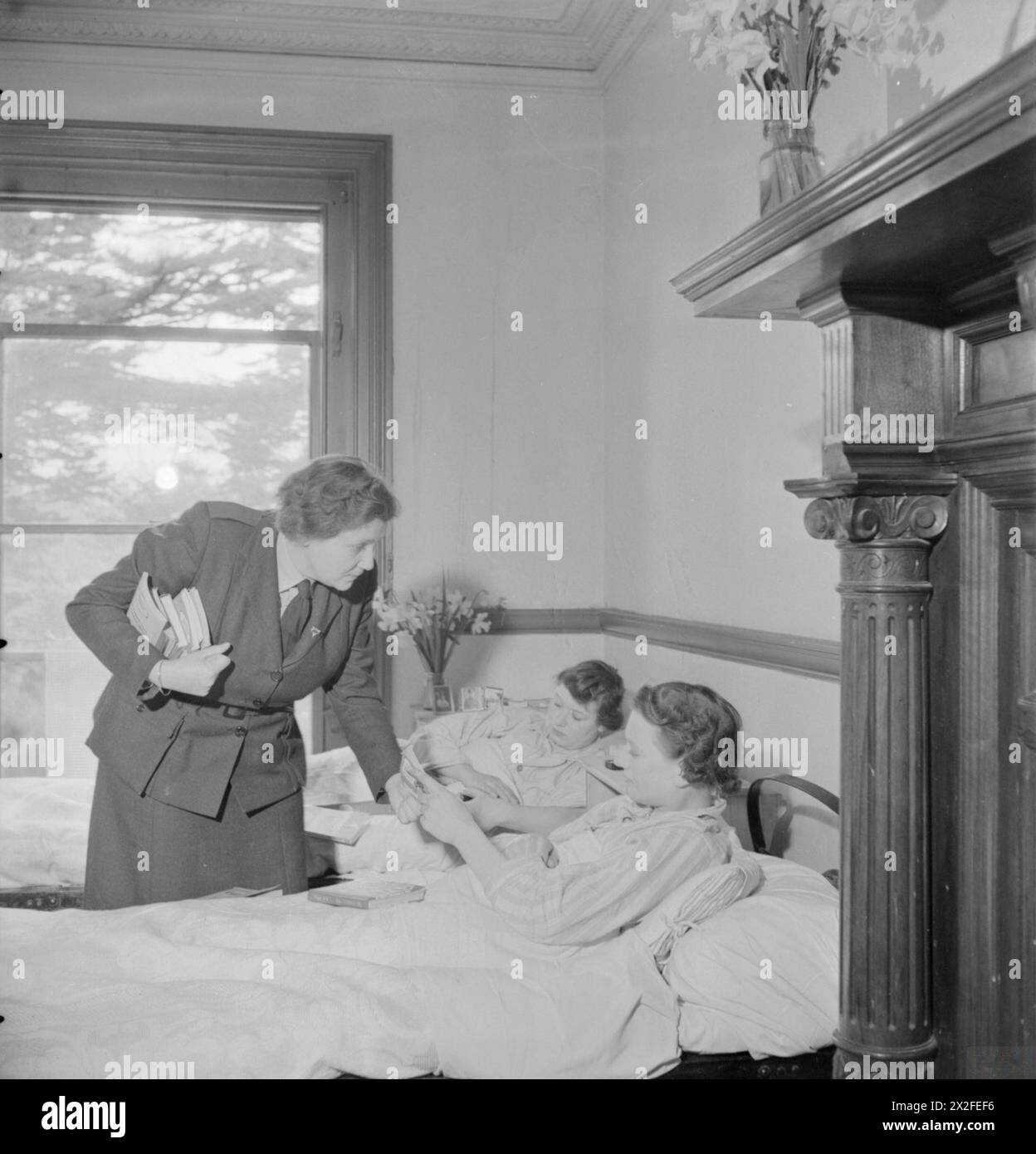 MOBILE CLUB : LE TRAVAIL DE LA CAMIONNETTE DU YWCA MOBILE CLUB EN GRANDE-BRETAGNE, 1943 - Kathleen Makower, organisatrice du club YWCA, rend visite aux membres de l'ATS à l'hôpital pour leur apporter des livres. Les patients sont le soldat Gladys Cooper (à droite), chauffeur de transport motorisé, et le soldat Edith Cox, opérateur de standard qui se remet d'une commotion cérébrale de l'Armée britannique, Service territorial auxiliaire Banque D'Images