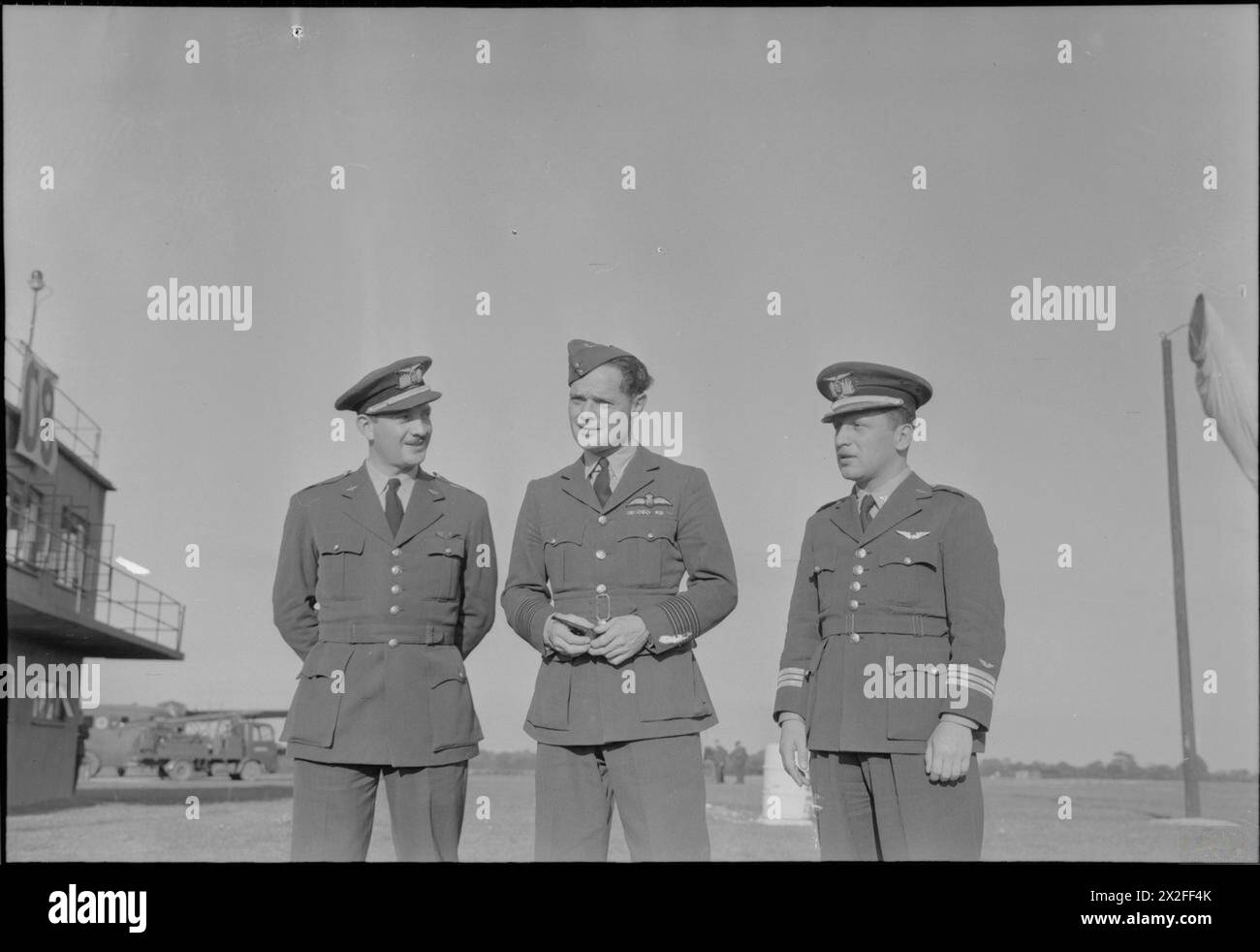 VISITE DE LA MISSION PÉRUVIENNE DES SERVICES COMBINÉS À LA STATION DE CHASSE DE BENTWATERS PRÈS DE WOODBRIDGE, SUFFOLK, ANGLETERRE, Royaume-Uni, 1945 - Flight Lieutenant M Burgos (à gauche) et chef d'escadron M O'Brien (à droite), tous deux du Pérou, discutent avec le capitaine de groupe Douglas Bader, DSO and Bar, DFC and Bar, lors d'une visite à RAF Bentwaters dans le Suffolk. À gauche de la photo, une partie des bâtiments de la tour de contrôle est visible, et la chaussette à vent est visible à droite de la photo Bader, Douglas Robert Steuart Banque D'Images