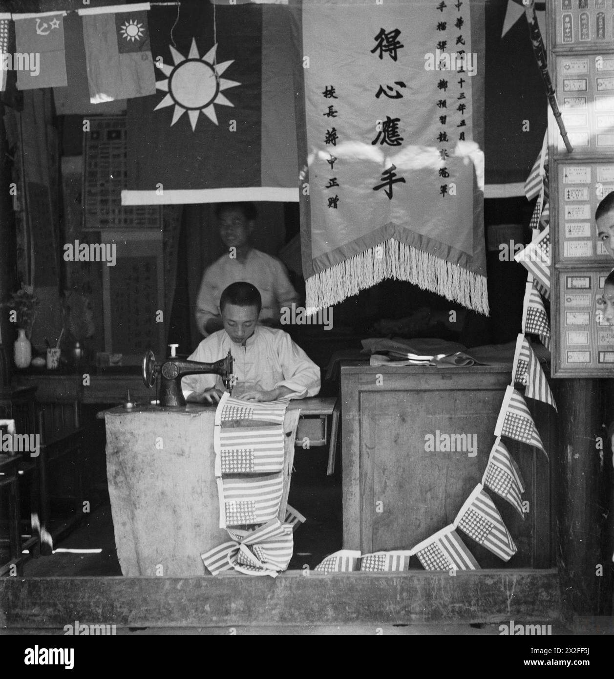 Un artisan chinois coud une chaîne de petits drapeaux américains dans sa boutique de Chengtu, en Chine, en 1944. Banque D'Images