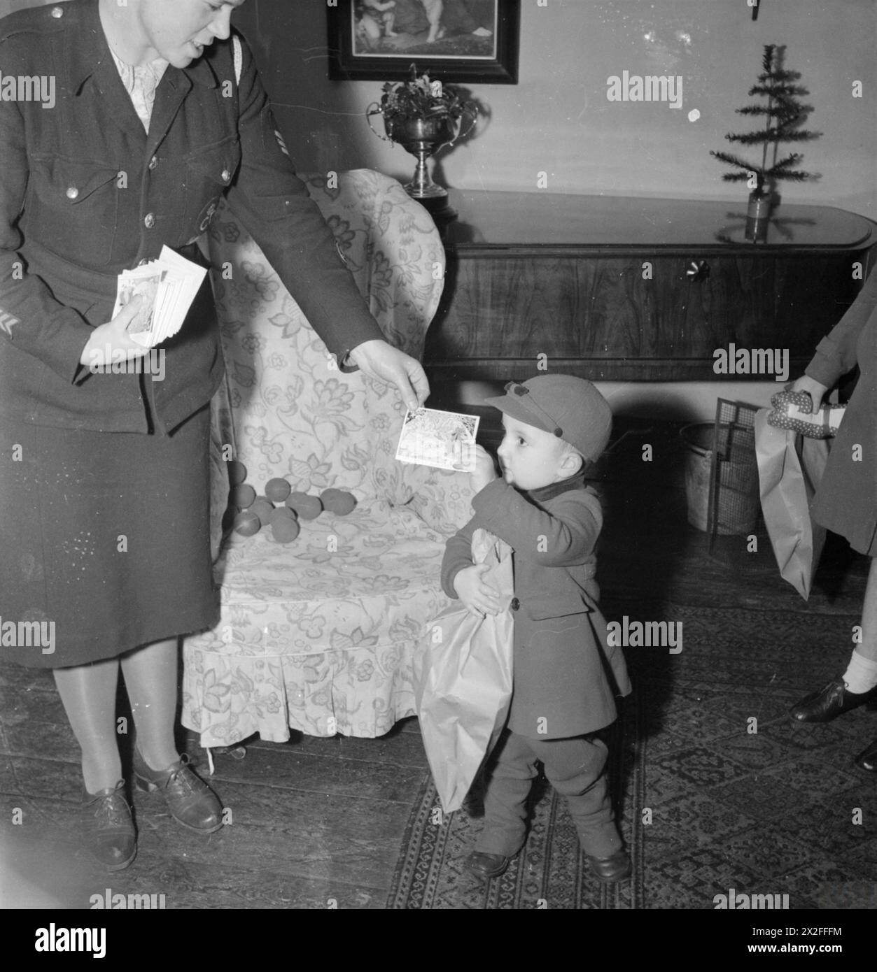 CADEAUX DE NOËL BWR DISTRIBUÉS AUX EAST ENDERS de LONDRES : AMERICAN AID TO THE CANNING TOWN SETTLEMENT, LONDRES, ANGLETERRE, Royaume-Uni, DÉCEMBRE 1944 - à la Settlement de Canning Town, Derek Cunningham reçoit une carte de Noël et un timbre d'épargne. En outre, il tient un sac en papier contenant un nouveau jouet et quelques bonbons, donnés comme cadeaux de Noël par l'Amérique par l'intermédiaire de la British War relief Society Banque D'Images