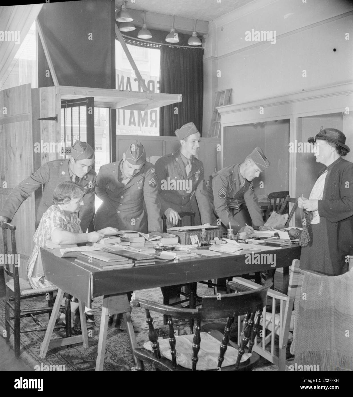 Quatre soldats américains visitent l'American information Bureau à Winchester, Hampshire, en 1944. Le bureau, dont le personnel est composé de femmes locales, fournit des conseils sur les activités et les sites touristiques de la ville. Les soldats comprennent le soldat T Branch, le caporal W Schimmel, le soldat P Schramm et le sergent d'état-major Edwin J Street. Banque D'Images